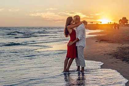 A photo of a couple hugging each other at the beach with the sun setting behind them