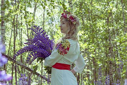 A russian woman holding a bouquet of flowers in a forest.